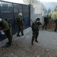 Five heavily armed soldiers stand in front of iron gate