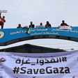 Banner reading #SaveGaza in English and Arabic hangs across checkpoint gate