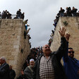 A man raising his hand surrounded by crowds with Bab al-Rahma gate in the background. 