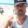 A man on a beach wears a baseball cap and smokes a cigarette