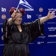 Woman dressed in black waves a blue and white flag in front of a backdrop featuring corporate logos. 