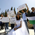 A young woman in a bridal grown sits in front of protesters holding signs