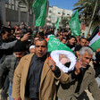 Walking men carry a body on a stretcher wrapped in a flag