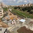 Hyundai bulldozers demolish home amid buildings and fields. 