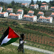 A Palestinian girl holds a Palestinian flag in front of a row of settlement houses.