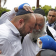 Two men, one with bandaged hands, embrace, as others look on.