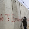 Man writes in red on an tall cement wall. 