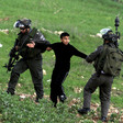 Two Israeli soldiers pull on the arms of a Palestinian youth.