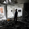 Man standing in bombed-out room looks up toward hole in ceiling
