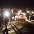 Armed police run in front of cars with the headlights on at night