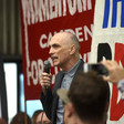 A man with a microphone addresses a crowd with signs