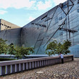 A man is dwarfed by a building that has many angles in its glass facade.