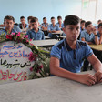 Boys sit in a classroom as a wreath with flowers and writing occupied one chair