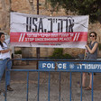 Two women hold sign reading "USA stop undermining peace" in English and Hebrew