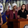 Three women stand around a fourth speaking at podium