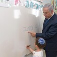 Man in suit looks over a child as he writes on whiteboard