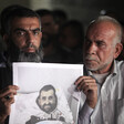  Two men, one of them holds an image of a man in a hospital bed 