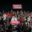 Man surrounded by crowd and signs speaks at podium