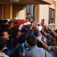 Body sheathed in flag is carried out of home by crowd of men