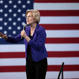 A woman with a microphone in front of American flag
