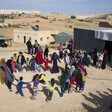 People dance in a circle near building structures 