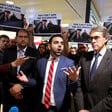 Man turns palms of his hands upwards as people around him hold placards