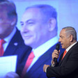 Benjamin Netanyahu speaks into a microphone in front of a picture of himself with US president Donald Trump