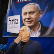 Man wearing a mask stands in front of Netanyahu banner