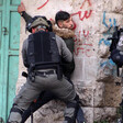 A soldier pins a young man against a stone wall