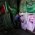 Man stands in front of stacked cartons with Palestinian and Saudi flags and portraits of Saudi royals displayed on them