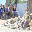 Boy wearing face mask sits on rubble with family in background
