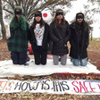 Blindfolded protesters kneel next to a banner.