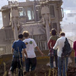 A group of people appears small next to an armored bulldozer