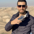 Man smiles and holds phone against backdrop of mountains