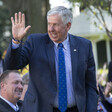 A man in a suit waves his hand