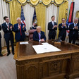 Man sits behind desk surrounded by men