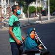 Man rolls woman on wheelchair, both wearing protective masks 