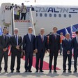 Men in suits stand in one line before airplane 