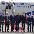 Men in suits stand in one line before airplane
