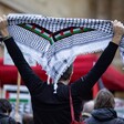 A man holds up a kuffiyeh scarf with a Palestinian flag inlay