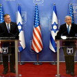 Two men stand at podiums with US and Israeli flags behind them