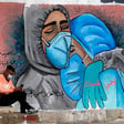 Man wearing mask sits on curb in front of mural showing doctors embracing
