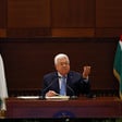 Mahmoud Abbas lifts hand in air while seated between two Palestinian flags