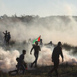 Protesters, one of them carrying a Palestine flag, are silhouetted against clouds of smoke