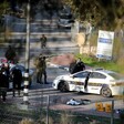 Covered body lies on road surrounded by police vehicles and uniformed personnel