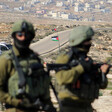 Two armed and uniformed soldiers stand in front of road