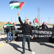 Man holds Palestine flag in air while standing in front of banner reading No to Apartheid No to Annexation