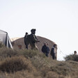 Soldier holding rifle stands in front of men on hilltop