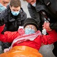 An activist in a mask being carried away by police in masks