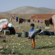 Boy stands near clothes line and scattered structures 